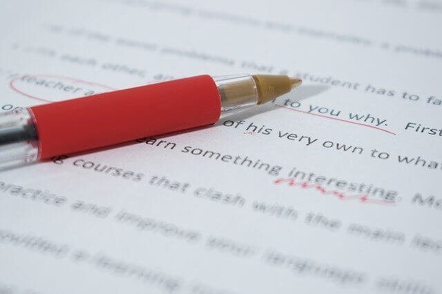 Image of a pen on a sheet of paper showing proofread, marked text